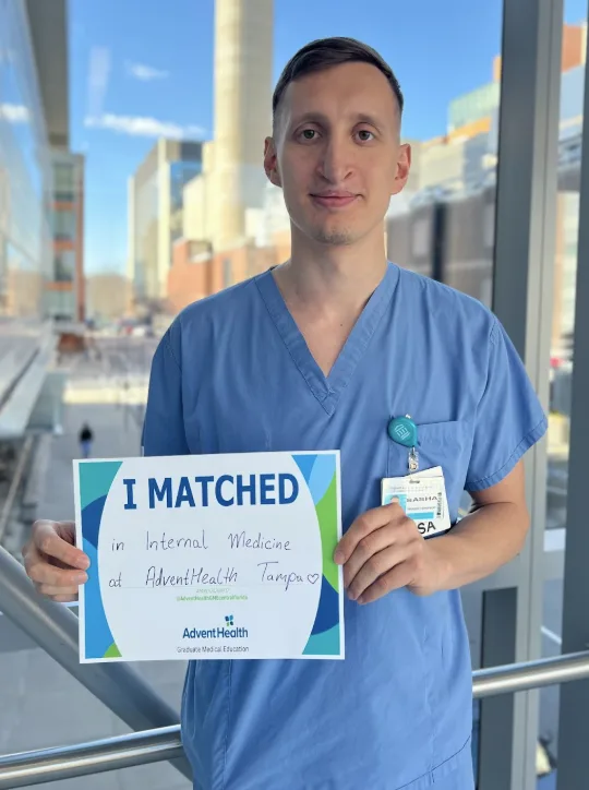 Sasha, a Ukrainian jobseeker, holding a sign saying "I matched in internal medicine at AdventHealth Tampa"